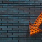 Bild mit Steinwand und orangebem Pfeil der nach unten zeigt
